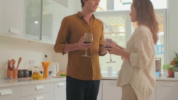 Średniej długości ujęcie młodej kochającej się pary spędzającej czas z winem i tańczącej stojąc w kuchni przed kolacją - Materiał filmowy, wideo
