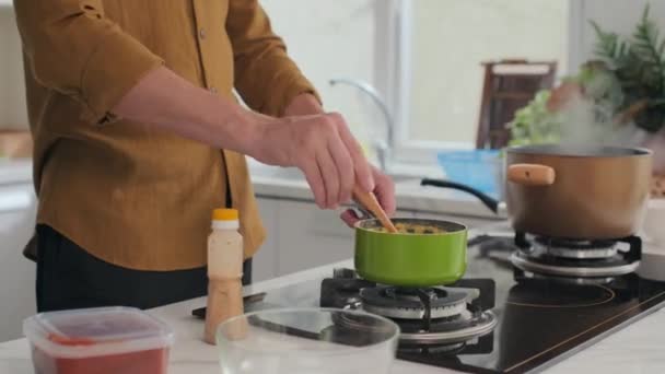 Rajattu laukaus mies sekoittaen sose vihreässä kattilassa kun ruoanlaitto illallinen keittiössä - Materiaali, video