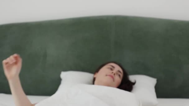  Νεαρή λευκή γυναίκα ξυπνάει και σηκώνεται στο κρεβάτι χαμογελώντας. Καλημέρα το Σαββατοκύριακο. Υγιής ύπνος σε ορθοπεδικό στρώμα - Πλάνα, βίντεο