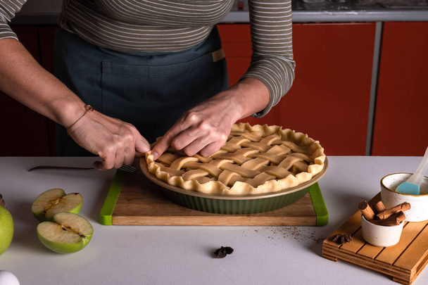 Женщина кладет пирожное тесто поверх яблочного пирога в булочную, готовое к запеканию в духовку, готовит яблочный пирог. Подготовка торта ко Дню Благодарения, осенняя пекарня. Хрустящие погодные сладости. Рецепт - Фото, изображение