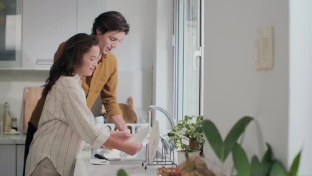 Середній довгий знімок молодої веселої пари пральних машин в раковині після вечері вдома - Кадри, відео