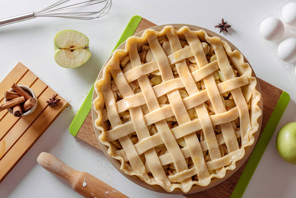 Неварений яблучний пиріг у випічці, готовий до приготування на білому кухонному столі, оточеному інгредієнтами. Концепція домашньої кухні, традиційний рецепт пирога для подяки, спосіб життя, вид зверху - Фото, зображення