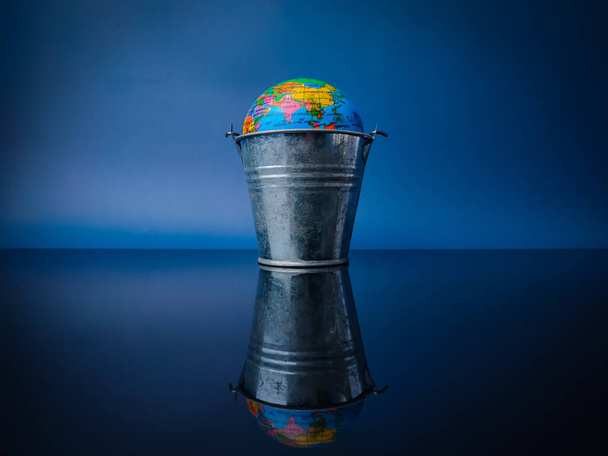 globe terrestre dans un seau en acier avec réflexion sur un panneau acrylique noir - Photo, image