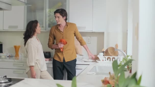 Medium long shot of loving wife cuddling her husband wiping plates after dinner standing at kitchen at home - Footage, Video