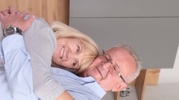 Handsome pensioner husband and wife are dancing, embracing, in the middle of the kitchen. Grandfathers love for grandmother. Vertical video - Metraje, vídeo