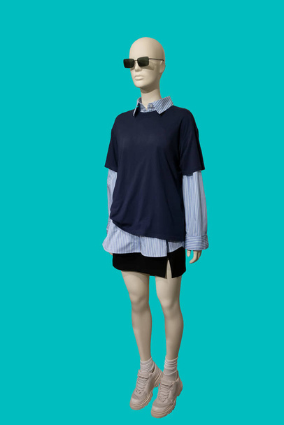Full length image of a female display mannequin wearing dark blue pullover with short sleeves, striped shirt and black mini skirt Isolated on green background - Photo, Image