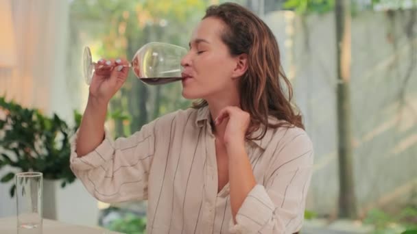 Portret van een jonge glimlachende vrouw die thuis wijn drinkt en naar de camera kijkt - Video