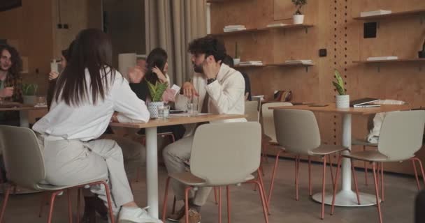 Verschillende groepen mensen bespreken projectdetails apart op verschillende tafels in de cafébar op kantoor, camera trucking beweging - Video