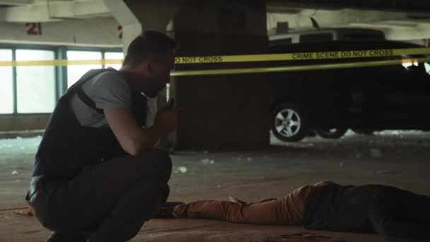 Середній повнометражний знімок кавказького детектива чоловічої поліції в куленепробивному жилеті, що йде навколо місця злочину, дивлячись на труп, розмовляючи на портативне радіо, і дивлячись на докази з експертом-криміналістом - Кадри, відео