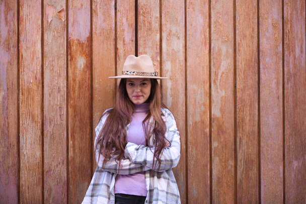 Jonge en mooie Spaanse vrouw uit Sevilla met bruin haar, hoed en geruit shirt op een houten deur in verschillende houdingen en uitdrukkingen. - Foto, afbeelding