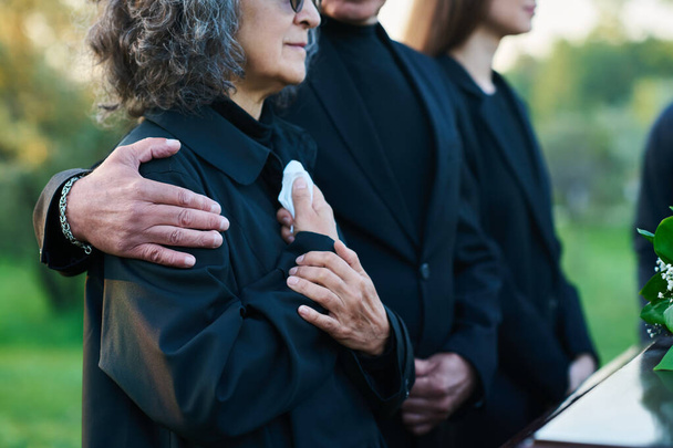 Hand van volwassen man op de schouder van zijn vrouw of zus met zakdoek treurend overlijdt familielid of familielid tijdens de begrafenis - Foto, afbeelding