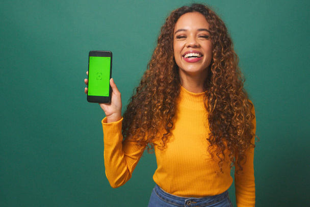 Ευτυχισμένη νεαρή γυναίκα κρατά μέχρι chroma οθόνη κλειδί συσκευή, πράσινο φόντο στούντιο. Υψηλής ποιότητας φωτογραφία - Φωτογραφία, εικόνα