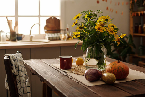 Composition of fresh wildflowers in vase or jar standing on wooden table with metallic mug, fresh ripe vegetables, lemons and linen napkin - Photo, Image