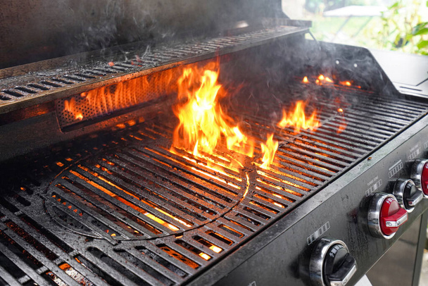 Η φωτιά ενός ψησταριά αερίου μαγειρεύει από το λίπος στη σχάρα σχάρα για να μαγειρέψουν το κρέας. - Φωτογραφία, εικόνα