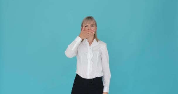 Confident woman with her hand covering her mouth, silencing herself, against a calming blue background. Her self-assured expression suggests a purposeful act of restraint or confidentiality. - Footage, Video