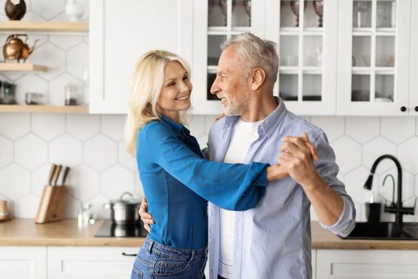 Portrait Of Loving Senior Couple Dancing Together In Kitchen Interior, Happy Romantic Elderly Spouses Having Fun, Holding Hands And Smiling To Each Other, Enjoying Spending Time At Home, Closeup Shot - Photo, image
