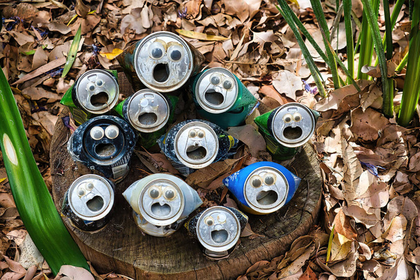 latas de aluminio bebida con los ojos y la boca abierta de pie en hojas secas. Concepto de reciclaje creativo. Varios colores y tamaños, concepto de inclusividad - Foto, Imagen