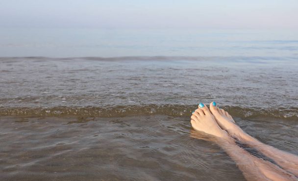 young woman with toenails with colored nail polish relaxing by the sea in summer - Photo, Image