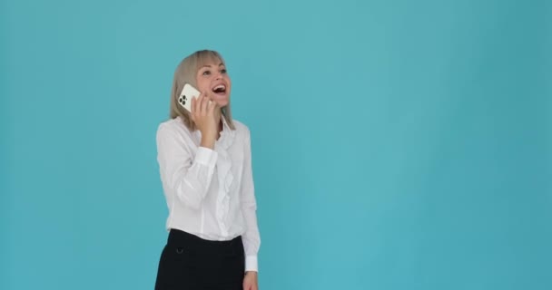 Mujer entusiasta se muestra teniendo una conversación animada en su teléfono sobre un fondo azul. Su expresión y gestos emocionados mientras habla transmiten su alegría y entusiasmo en la conversación. - Metraje, vídeo