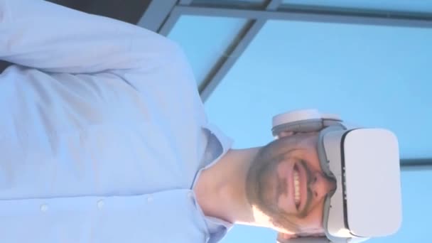 Un oficinista usa gafas de realidad virtual mientras está de pie cerca de un centro de negocios de vidrio. Tecnologías virtuales en los negocios. Vídeo vertical - Metraje, vídeo