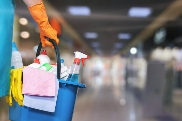 Une femme de ménage avec un seau et des produits de nettoyage sur fond de centre commercial flou. - Photo, image