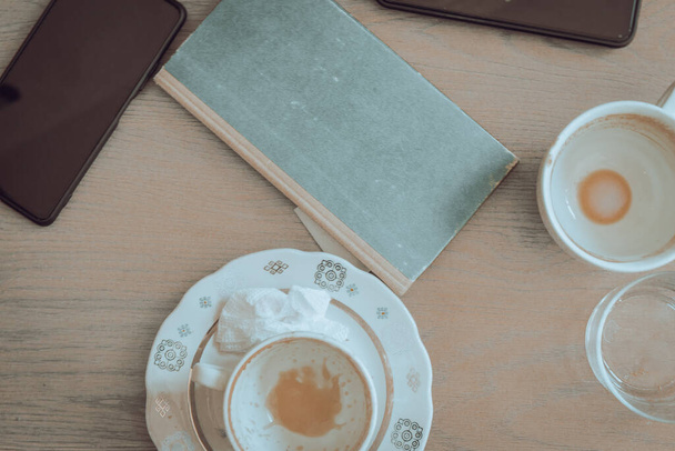 Dos tazas de café vacías, libro y teléfonos móviles en mesa de madera. Mesa de desayuno. Bebidas matutinas. Café interior. Estilo de vida urbano. Fondo de descanso de café. La vida cotidiana. Puesta plana. - Foto, imagen