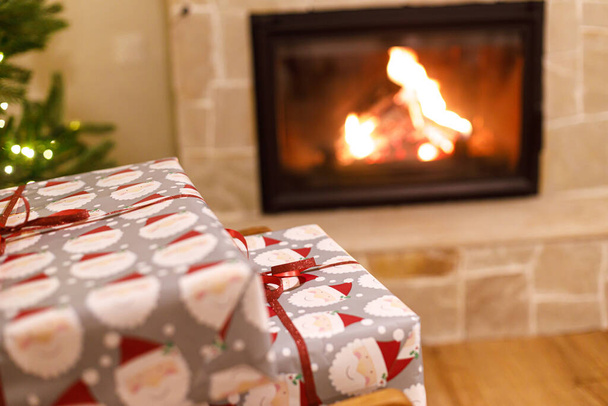 Joyeux Noël ! Cadeaux de Noël enveloppés élégants sur fauteuil contre l'arbre de Noël avec des lumières festives et cheminée à combustion confortable. Veille de Noël atmosphérique, temps des fêtes. - Photo, image
