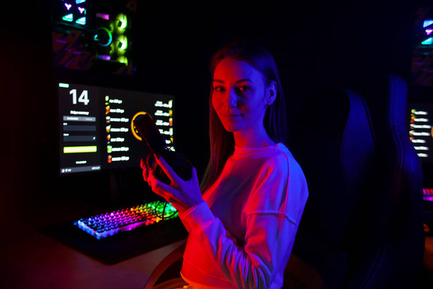young girl gamer sits in headphones in a computer club looks at the camera and smiles, portrait of a cybersports girl - Fotó, kép