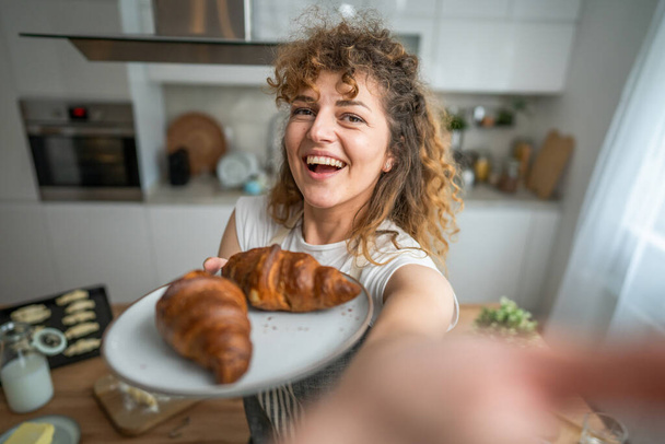 Одна взрослая белая женщина стоит на кухне со свежим круассаном на завтрак каждый день - Фото, изображение