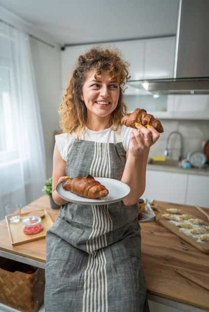 Egy felnőtt kaukázusi nő áll a konyhában friss croissant reggelire minden reggel rutin - Fotó, kép