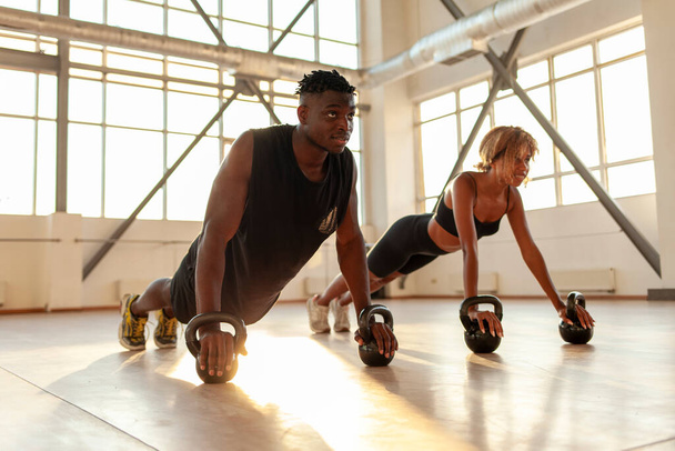 atlético casal afro-americano em uniformes esportivos treinar e fazer flexões no ginásio, homem treinador e mulher entrar para esportes na sala de fitness na parte da manhã - Foto, Imagem