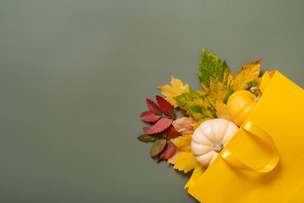 Herfst winkelen en verkoop platte lay concept. Samenstelling van herfst gevallen bladeren en een boodschappentas op een groene achtergrond. - Foto, afbeelding