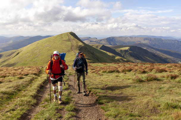 два чоловіки з пішохідним обладнанням і рюкзаками йдуть в гори з пішохідними стовпами на тлі ландшафту, туристи в окулярах піднімаються в гори разом - Фото, зображення