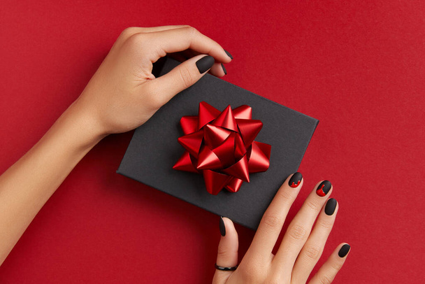 Beautiful groomed womans hands with gift box on red background. Halloween shopping sale concept. Manicure, pedicure beauty salon template - Photo, Image