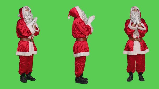 Радісні оплески персонажа на камеру, веселі за щось і чіпляються за руки на зеленому тлі. Санта-Клаус задоволений стоячим жестом овації, традиційним червоним костюмом. - Фото, зображення