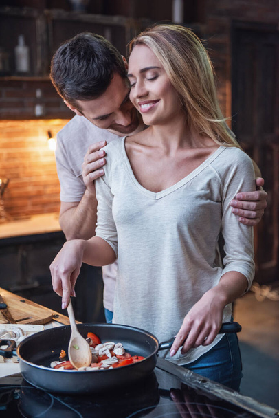 Jóképű férfi megcsókolta gyönyörű barátnője vállát, míg ő van a főzéshez - Fotó, kép