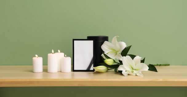 Urna mortuária com moldura de foto em branco, velas brilhantes e flores de lírio na mesa - Foto, Imagem