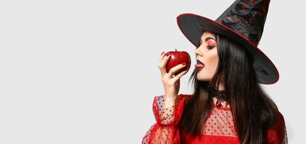Sexy young witch with poisoned apple on light background with space for text - Photo, Image