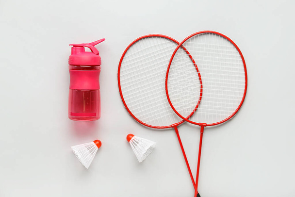 Badminton rackets, shuttledoppen en flesje water op lichte ondergrond - Foto, afbeelding