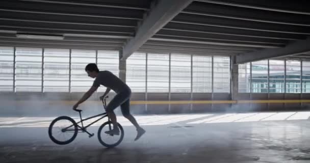 Pan ліворуч відстежуючий знімок велосипедиста, який виконує екстремальний трюк на BMX з однією ногою на кілочку та іншими гойдалками назад і вперед, щоб баланс тримався за руків'я та сидіння - Кадри, відео