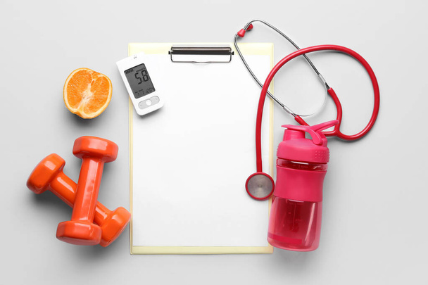Portapapeles en blanco con glucosímetro, naranja, mancuernas, botella y estetoscopio sobre fondo claro. Concepto de diabetes - Foto, Imagen