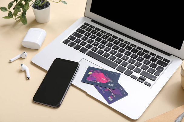 Computer portatile con carte di credito, telefono cellulare e auricolari su sfondo beige, primo piano. Shopping online - Foto, immagini