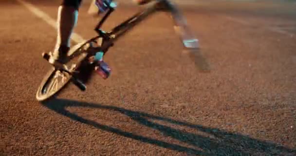 Duży kąt uchwyt handheld ziarna anonimowy sportowiec balansowanie na tylnym kole BMX z jednej nogi podczas ćwiczeń kaskaderskich na nocnej ulicy oświetlony latarnią - Materiał filmowy, wideo
