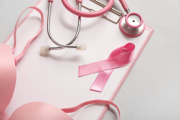 Pink ribbon with stethoscope, bra and clipboard on grey background. Breast cancer awareness concept - Photo, Image
