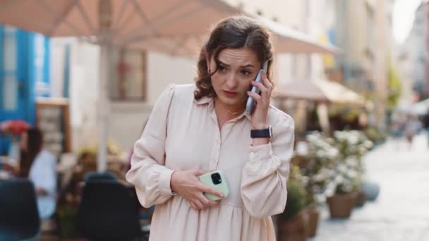 Irritée nerveuse stressée jeune femme parlant hurlant sur deux téléphones mobiles ayant conversation conflit querelle plainte différend discuter résoudre problème à l'extérieur. Fille marchant dans la rue urbaine - Séquence, vidéo