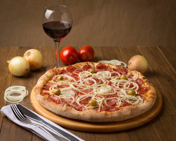 Pepperoni pizza s plátky cibule a zelené olivy. Sklenice červeného vína a rustikální cibule. Brazilské tipy. Podobná Pepperonieho pizze. - Fotografie, Obrázek