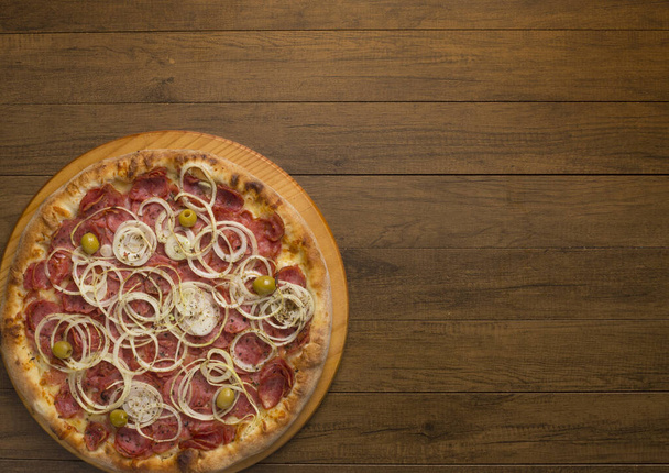 Foto de una pizza de pepperoni, rodajas de cebolla, queso mozzarella y aceitunas verdes. Fotografía horizontal. Fotografía gastronómica de primer nivel, con espacio para textos. Comida a la izquierda. - Foto, imagen