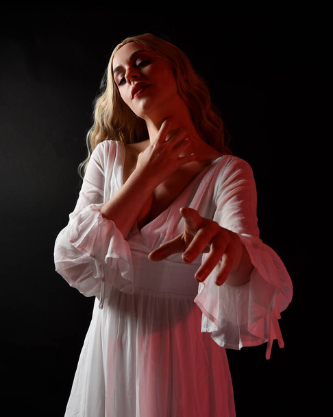 Κοντινό πορτρέτο της τρομακτικής ξανθιάς νύφης βαμπίρ φορώντας κομψό λευκό αποκριάτικο φόρεμα φαντασίας. Απομονωμένα σε σκοτεινό φόντο στούντιο με αγχώδη χέρια gestural φτάσει έξω  - Φωτογραφία, εικόνα