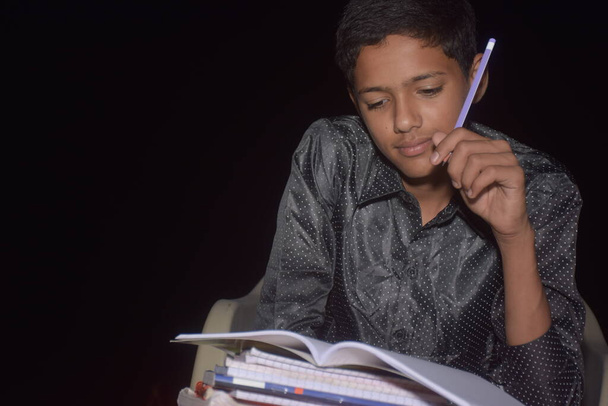 αγόρι στο σπίτι κάνει την εργασία και τη μελέτη, γράφοντας με ένα μολύβι σε ένα σημειωματάριο, τη νύχτα - Φωτογραφία, εικόνα