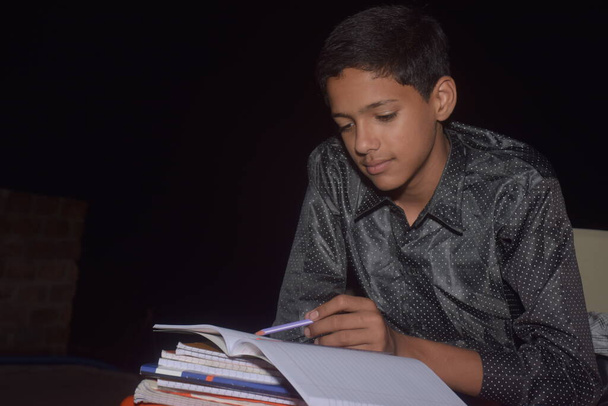 мальчик дома делает домашнюю работу и учится, пишет карандашом в блокноте, ночью - Фото, изображение